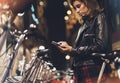 Young girl in black leather jacket using smartphone on background illumination glow bokeh light in night atmospheric christmas Royalty Free Stock Photo