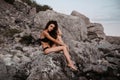 young girl in a black swimsuit is sitting sexy on rocks on the beach by the sea in summer Royalty Free Stock Photo