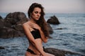 young girl in a black swimsuit is sitting sexy on rocks on the beach by the sea in summer Royalty Free Stock Photo