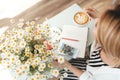 Girl with blond hair sitting in cafe with cup of coffee and bouquet of little chamomile on table