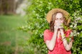 Young girl blowing nose and sneezing in tissue in front of blooming tree. Seasonal allergens affecting people. Beautiful lady has