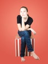 Young girl in a blue jeans and black T-shirt sits on a red striped box