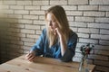 Young girl in blue shirt sits at table in headphones and thought Royalty Free Stock Photo