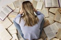 A young girl in a blue sweater and jeans sits on a pile of open books clutching her head in her hands. Back view. Education and Royalty Free Stock Photo