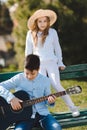 Young girl and boy with the guitar sitting at the bench in park. Children love