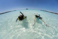 Young girl and boy snorkeling in crystal clear water with cruise ship in background with wide angle curved horizon.