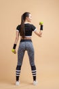 A young girl, brunette with a ponytail, shakes her biceps, holds a green dumbbell in her hand, bending her elbow.