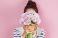 Young girl with bun hairstyle wearing striped pullover smelling hiding head in bouquet of double tulip flowers on pastel pink