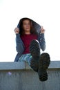 A young girl in camouflage pants and berets sits on a high granite stone wall with her legs dangling over the blue sky. Royalty Free Stock Photo