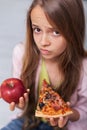 Young girl cannot decide between appetizing pizza and healthy apple