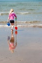 A young girl carries a bucket and spade to the shoreline on a beach