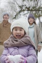 Young girl carrying snow balls in front of parents in park in winter