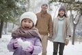 Young girl carrying snow balls in front of parents in park in winter