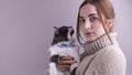 A young girl with a cat in her arms near a gray wall. Beautiful fluffy domestic cat in a collar. Love with pets. Copy