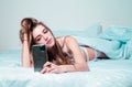 Young girl chatting on phone in the morning in bed. Woman in bed checking social apps with smartphone. Royalty Free Stock Photo