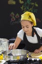 Young girl in a chef`s hat cooks in a large saucepan in a black Royalty Free Stock Photo