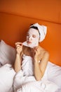 Young girl with clean skin with a mask on her face, sitting in bed, resting after a shower, relaxing at home. Close-up Royalty Free Stock Photo