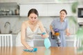 Young girl cleaning the table surface, mother vacuum-cleaning in the kitchen