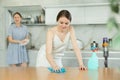 Young girl cleaning the table surface, mother wiping plates in the kitchen