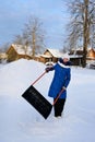 young girl cleans snow with shovel in countryside. Teenage girl with large scraper helps adults to remove snow. Royalty Free Stock Photo