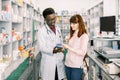 Young girl client who is satisfied of recommended medicines in pharmacy, while standing together with African man