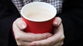 A young girl in a coat holds morning coffee with her while walking in the park. Hand holding paper cup of coffee in green park.