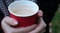 A young girl in a coat holds morning coffee with her while walking in the park. Hand holding paper cup of coffee in green park. Royalty Free Stock Photo