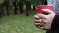 A young girl in a coat holds morning coffee with her while walking in the park. Hand holding paper cup of coffee in green park.