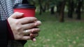 A young girl in a coat holds morning coffee with her while walking in the park. Hand holding paper cup of coffee in green park.