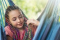Young girl with colorful braids in her hair is resting on blue hammock Royalty Free Stock Photo