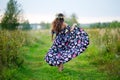 Young girl in a colorful sundress with a wreath on her head goes away along a road