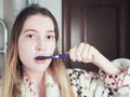 A young girl with cream on her face brushes her teeth with a toothbrush