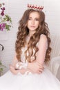 Young girl in the crown and white dress in the studio on a light background