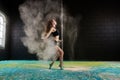 Young girl is dancing at a pole at a hall with colorful floor background with a dust powder in motion