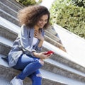 Young girl with dark curly hair using phone in a city park. Royalty Free Stock Photo