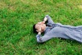 A young girl with dark short hair is lying on the green grass, covering her eyes with her hands