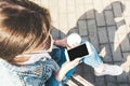 A young girl in a denim jacket walks down the street with coffee and a phone in her hands. Girl in glasses and a denim jacket on