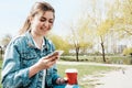 A young girl in a denim jacket walks down the street with coffee and a phone in her hands. Girl in glasses and a denim jacket on