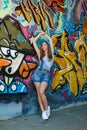 Girl in denim overalls posing against wall with graffiti