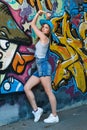 Girl in denim overalls posing against wall with graffiti