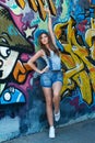 Girl in denim overalls posing against wall with graffiti