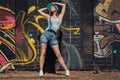 Girl in denim overalls posing against wall with graffiti