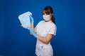 A young girl doctor in a medical mask holds a lot of masks in her hands. A nurse poses on a blue background