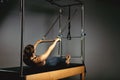 A young girl does Pilates exercises with a bed reformer, barrel machine tool. Beautiful slim fitness trainer on the