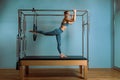 A young girl does Pilates exercises with a bed reformer, barrel machine tool. Beautiful slim fitness trainer on the