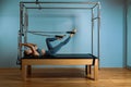 A young girl does Pilates exercises with a bed reformer, barrel machine tool. Beautiful slim fitness trainer on the