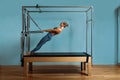 A young girl does Pilates exercises with a bed reformer, barrel machine tool. Beautiful slim fitness trainer on the