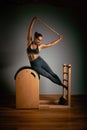 A young girl does Pilates exercises with a bed reformer, barrel machine tool. Beautiful slim fitness trainer on a