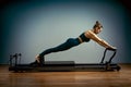 Young girl doing pilates exercises with a reformer bed. Beautiful slim fitness trainer on reformer gray background, low