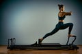 Young girl doing pilates exercises with a reformer bed. Beautiful slim fitness trainer on a reformer gray background